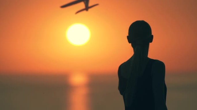 那个女人把玩具飞机扔在日落背景上。慢动作