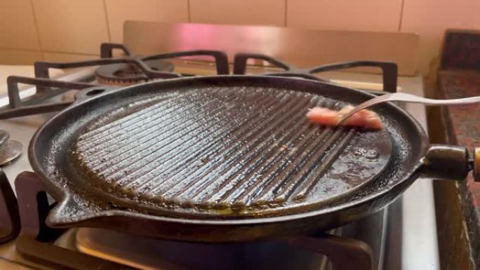 女人用一块脂肪给铸铁锅上油或上油，以防止肉粘在铸铁上。特写。4k分辨率。