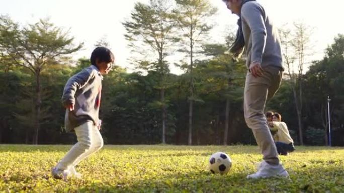 亚洲小男孩在公园与父亲在户外踢足球