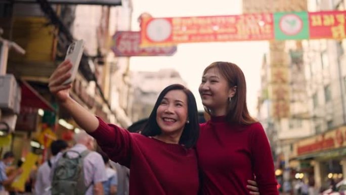 在中国城镇地区的农历新年灯笼上使用电话的亚洲妇女