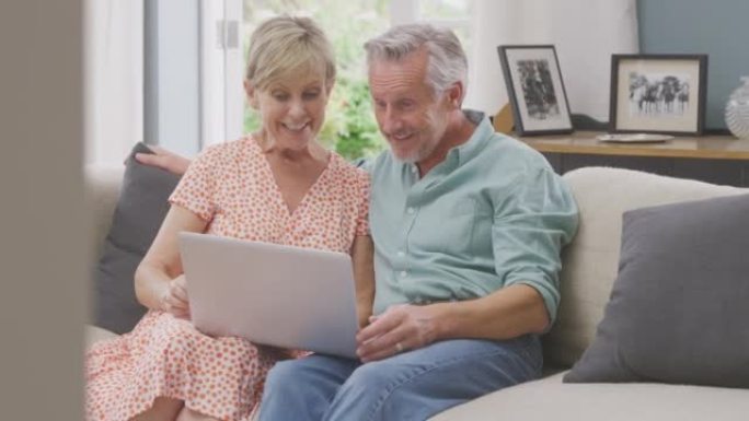 资深退休夫妇坐在家里的沙发上，用笔记本电脑进行视频通话