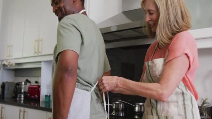 多样化的高级夫妇在厨房准备食物之前先穿上围裙