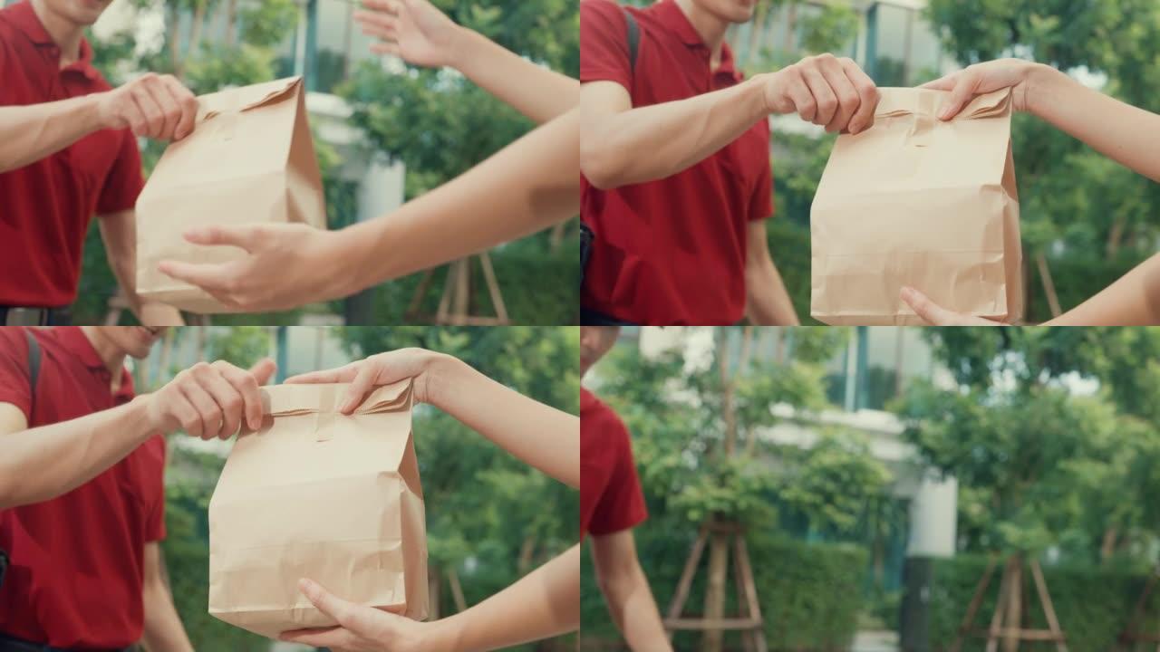 特写年轻快乐的亚洲送货员，穿着红色制服的自行车，携带箱子敲门回家网上购物食品纸袋给在家门前的女人。