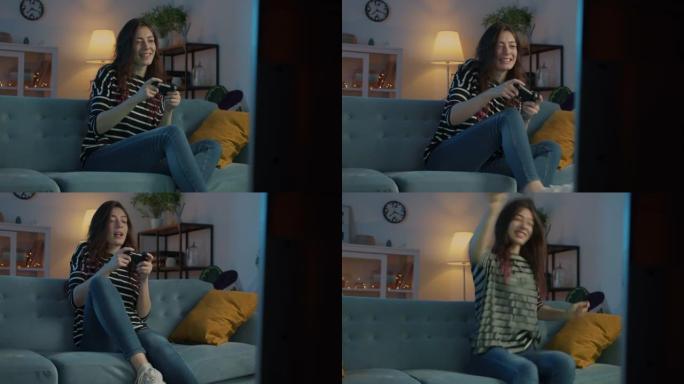 年轻漂亮的女孩晚上坐在现代公寓的沙发上在家享受电子游戏