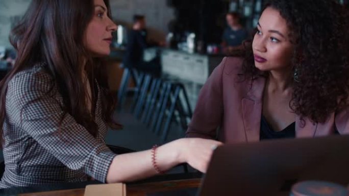 面试概念。两名年轻漂亮的多民族妇女使用笔记本电脑交谈，在咖啡馆商务午餐会上一起工作。