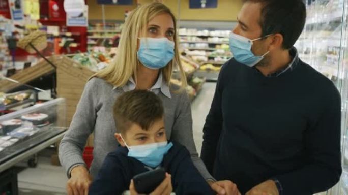 父亲，母亲和儿子的幸福家庭的真实照片戴着医用口罩，以保护自己免受疾病的侵害，同时在超市一起购买杂货。