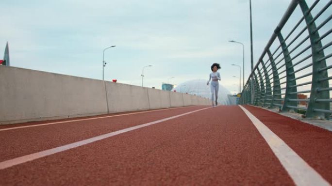 一个穿着黑色卷发的白色紧身裤的年轻健美女正在桥上慢跑