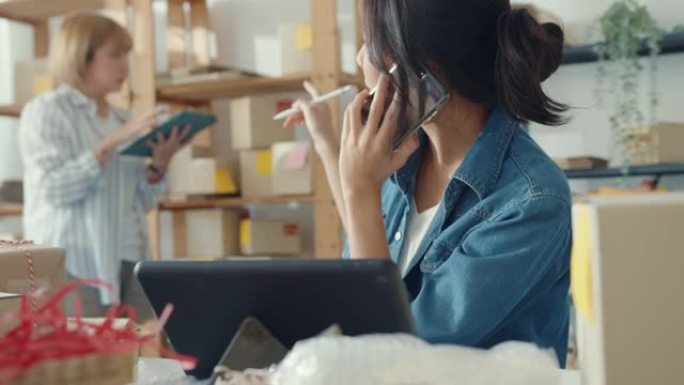 年轻的亚洲女企业家使用手机电话接收采购订单，并在家庭办公室检查库存工作的产品。小企业主，在线市场交付