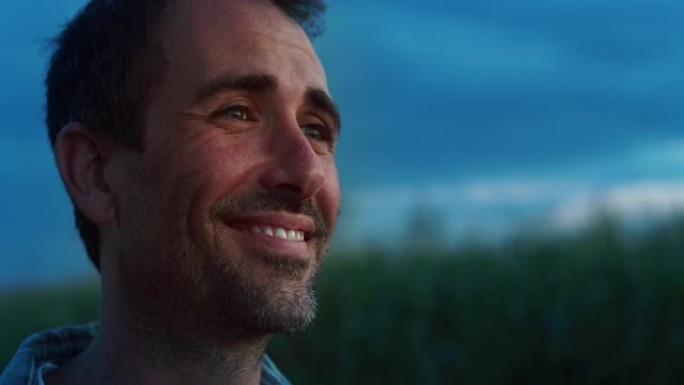 一个快乐的人的肖像在一片充满玉米作物的绿色田野里摆姿势，微笑着。英俊的中年男性农民在农村享受工作和生