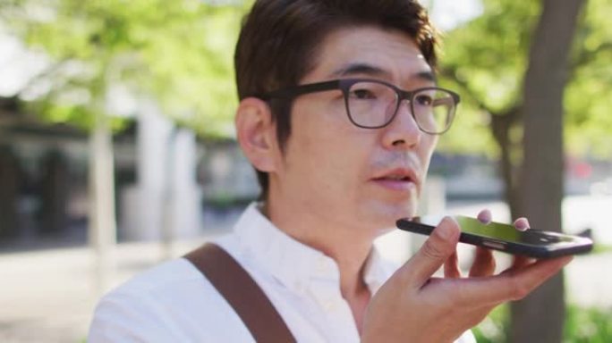 亚洲男子站在街上时在智能手机上聊天的特写
