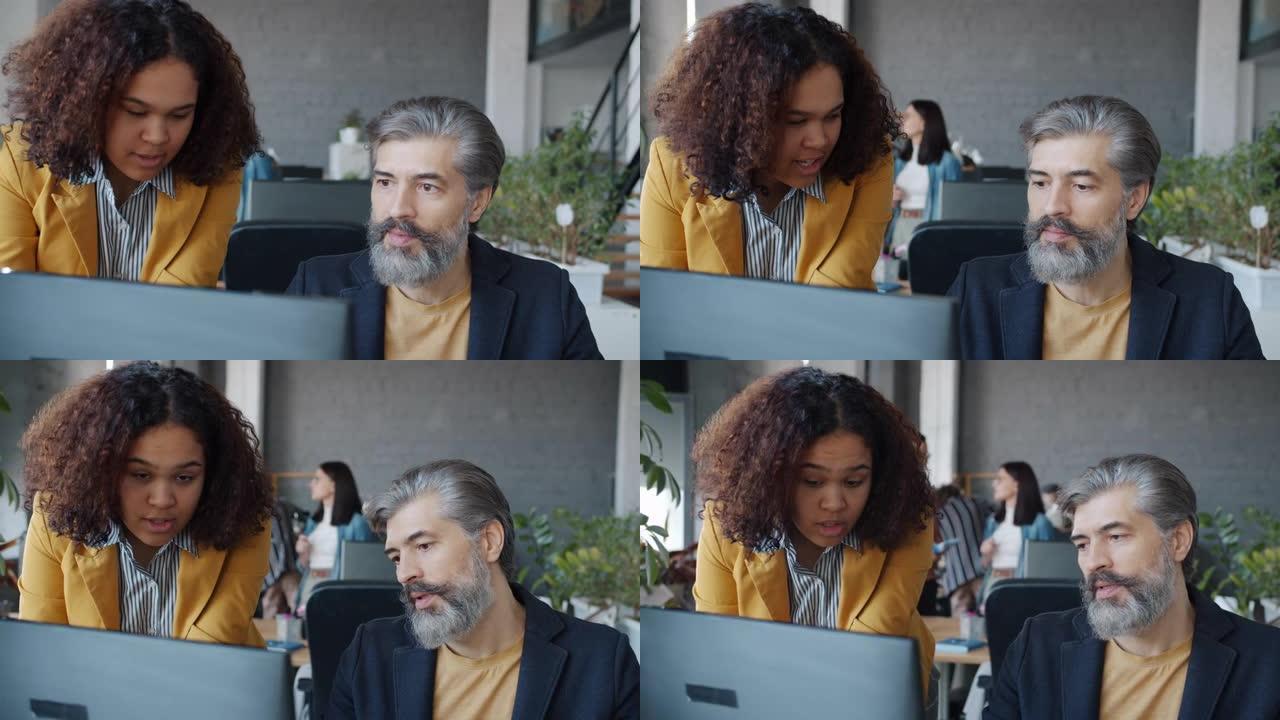 非裔美国妇女和白人男子在共享办公室使用计算机交谈
