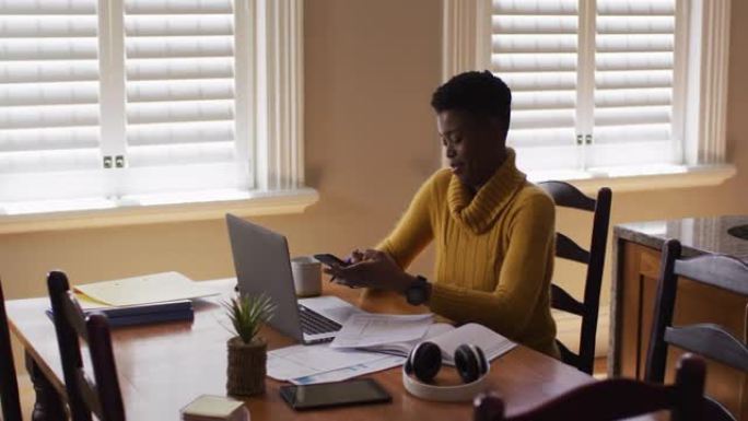 非裔美国妇女在家工作时在智能手机上聊天并使用笔记本电脑