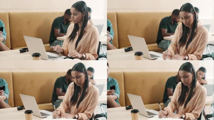 专注于创意的女商人在笔记本电脑上打字，在办公室的笔记本上写笔记。年轻的拉丁裔设计师坐着，工作和计划策