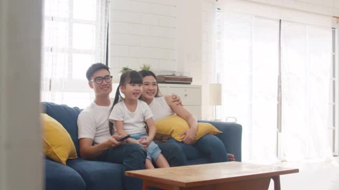 快乐的亚洲家庭享受他们的空闲时间在家里一起放松。生活方式韩国爸爸、妈妈和女儿一起看电视，躺在现代房子