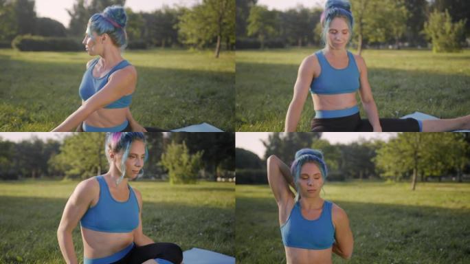 迷人的年轻女子，蓝色的头发，穿着蓝色的瑜伽服，在公园的草地上做瑜伽，在日出或日落时，通过左右转动来伸