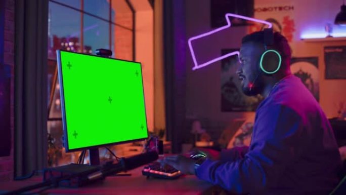 兴奋的玩家玩在线视频游戏，在他功能强大的个人电脑上模拟绿屏。房间和电脑有彩色霓虹灯。阁楼公寓舒适的夜