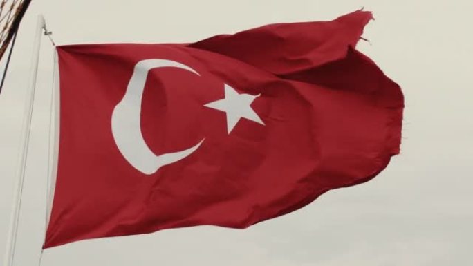 美丽的土耳其国旗的低角度特写，在灰色多云的天空背景下，国家标志在大风中挥舞着杆子。