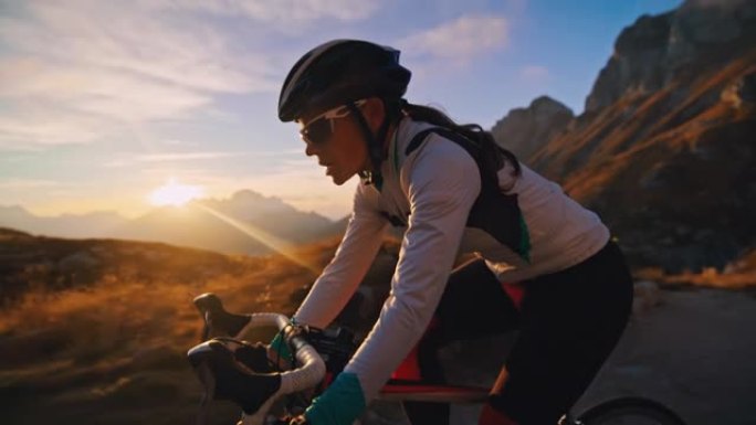 女自行车手在日出时在阳光明媚的山路上坡骑行