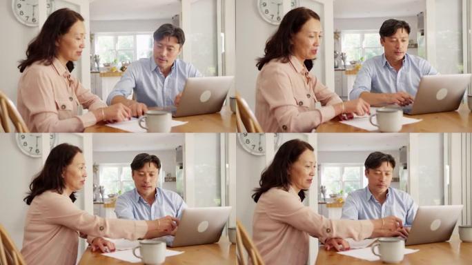 成熟的亚洲夫妇坐在家里的餐桌旁，用笔记本电脑整理家庭账单和财务 -- 慢动作拍摄