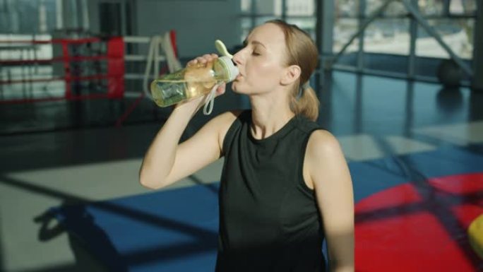 有吸引力的女运动员在健身房里拿起水瓶喝酒享受休息