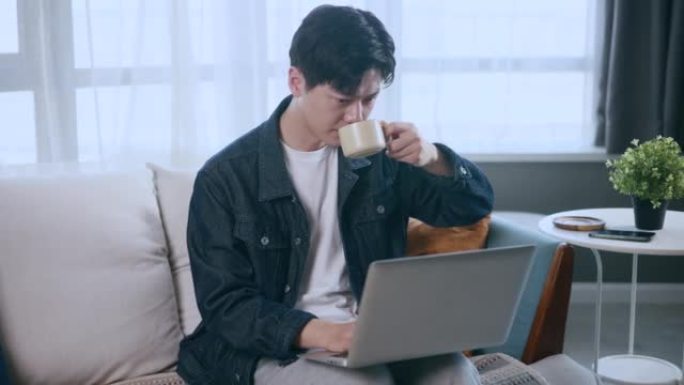 亚洲男子在家喝咖啡和用笔记本电脑工作