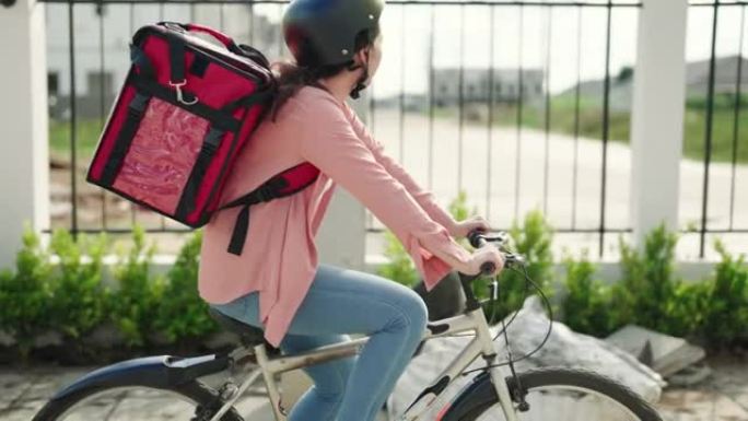 食品配送快递员穿着红色保暖背包骑着自行车在路上为客户配送订单