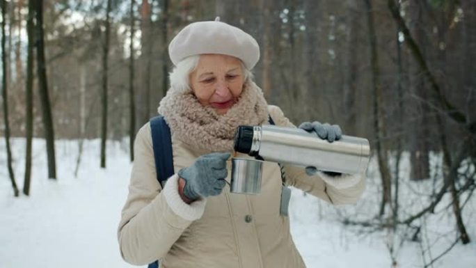冬季，老年游客在森林里从热水瓶里倒热茶的慢动作