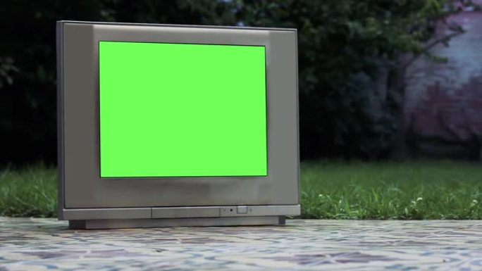 旧灰色电视在房子的后院里有绿屏。