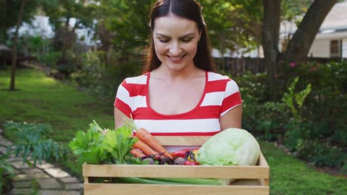 微笑的白人妇女站在花园里拿着一盒蔬菜