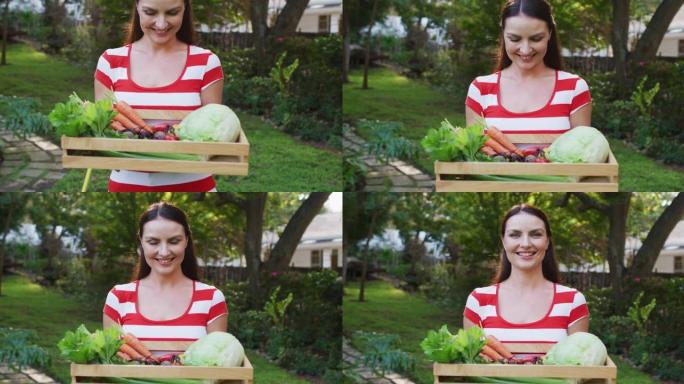 微笑的白人妇女站在花园里拿着一盒蔬菜