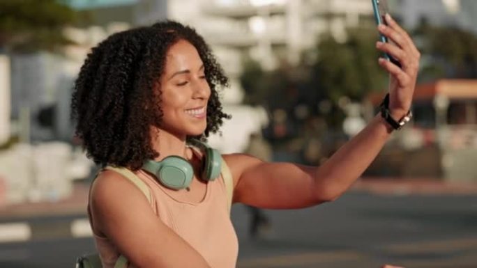 自拍，黑人妇女和电话在户外戴着耳机在城市里开心，交流和微笑。女士，女孩和智能手机进行视频通话，放松和