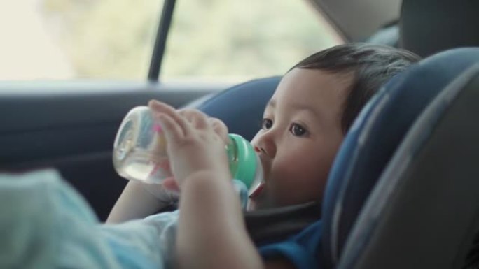 亚洲小男孩从汽车座椅上的瓶子里喝水