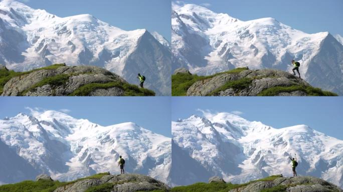 男子徒步旅行者爬上山顶，用全景雪山举起双臂向天空