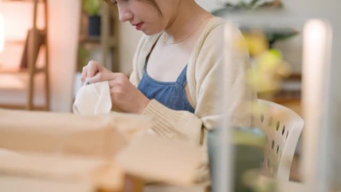 年轻的亚洲女性从她在家网上购物零售送货的纸板箱中拆箱新购买的衣服。