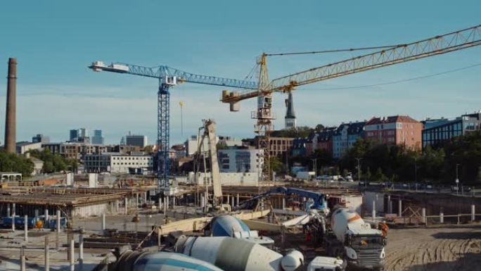 高空飞行在新的建筑开发场地上，用高塔起重机建造房地产。雇用重型机械和建筑工人。背景中的城市房屋。