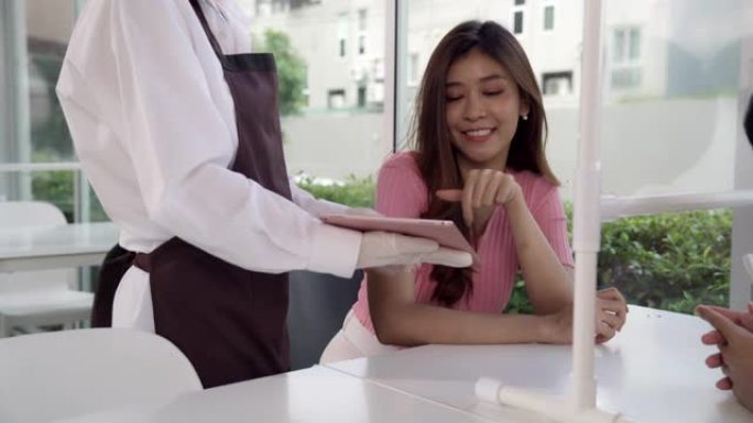 4K UHD多莉镜头: 女服务员使用数字平板电脑向情侣顾客展示和推荐菜单。新的正常生活方式技术和非接