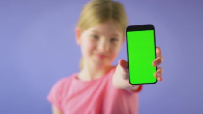 微笑女孩拿着绿屏手机在紫色工作室背景下看着相机的工作室镜头-慢动作拍摄
