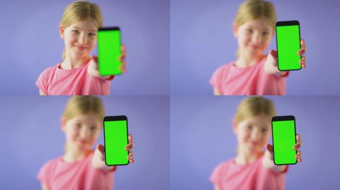 微笑女孩拿着绿屏手机在紫色工作室背景下看着相机的工作室镜头-慢动作拍摄