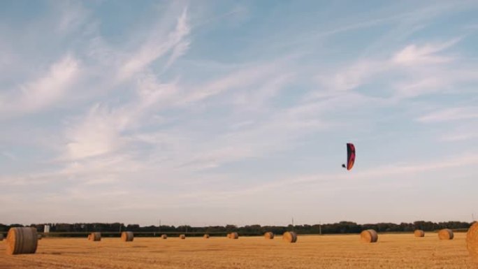慢动作手持拍摄的滑翔伞飞越装满吨包的收获的农田