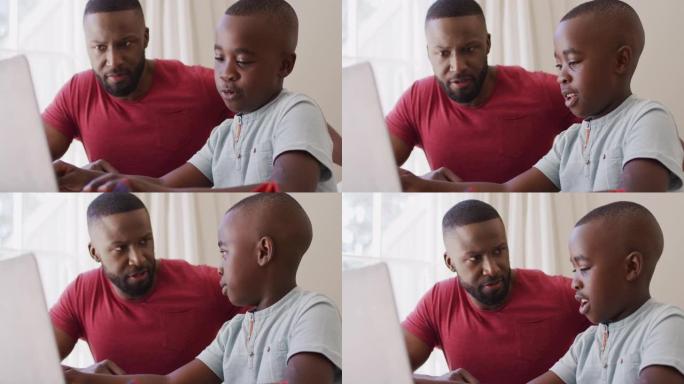 非裔美国父亲在坐在家里帮助儿子使用笔记本电脑