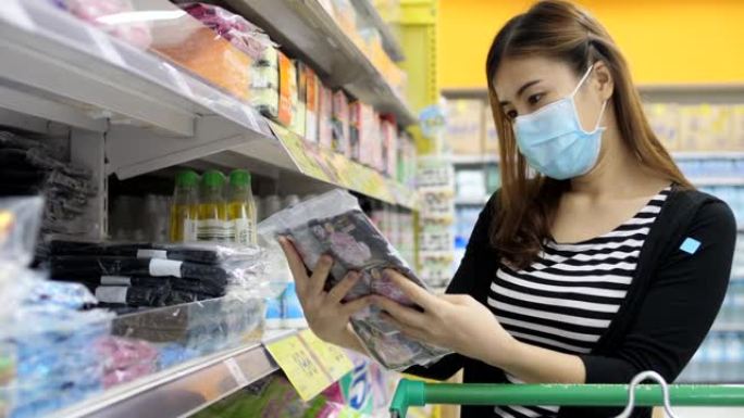 年轻的亚洲妇女带着防护口罩在超市购物，阅读清单