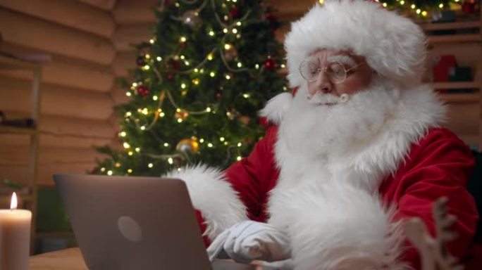 戴着白手套的圣诞老人正坐在他的办公室里，在他的笔记本电脑里打字