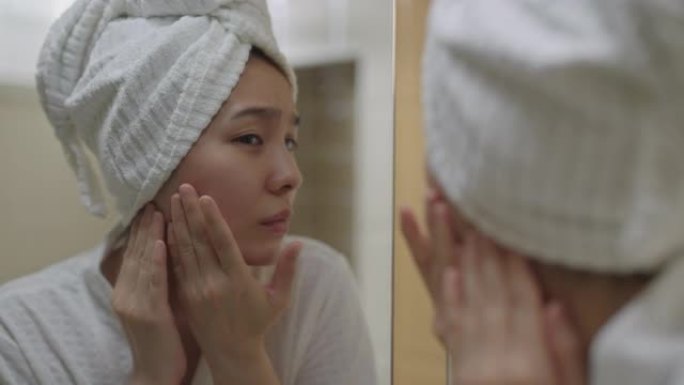 年轻女子在家里的浴室镜子里看着自己的脸时感到沮丧
