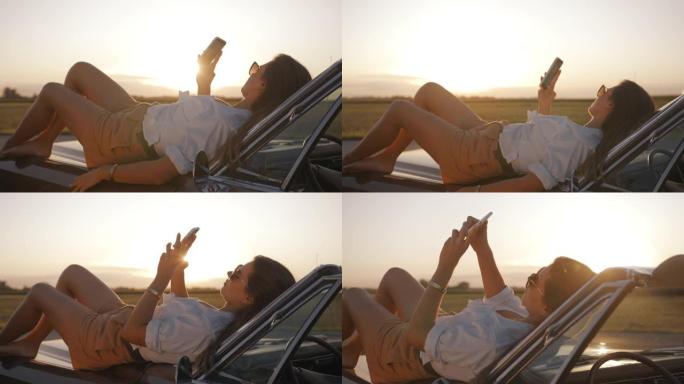 SLO MO年轻女子躺在汽车引擎盖上时使用智能手机