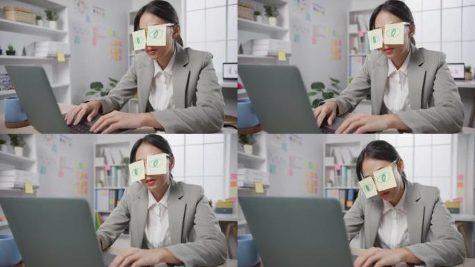 年轻的亚洲女商人坐在办公桌上劳累劳累，睡在办公室的笔记本电脑上。