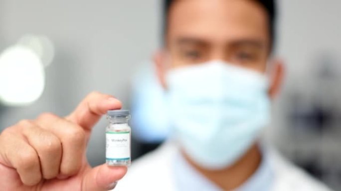医生在模糊的背景下拿着疫苗用于病毒或covid。一位医学研究人员戴着口罩并在实验室展示了注射流感的玻