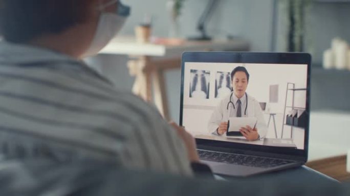 年轻的亚洲女孩戴防护口罩使用笔记本电脑在家里客厅与高级医生在线咨询视频通话中谈论疾病。