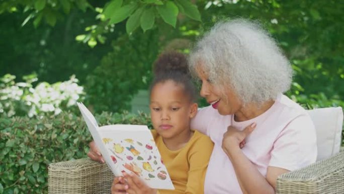 祖母坐在户外花园里，孙女在家一起看书