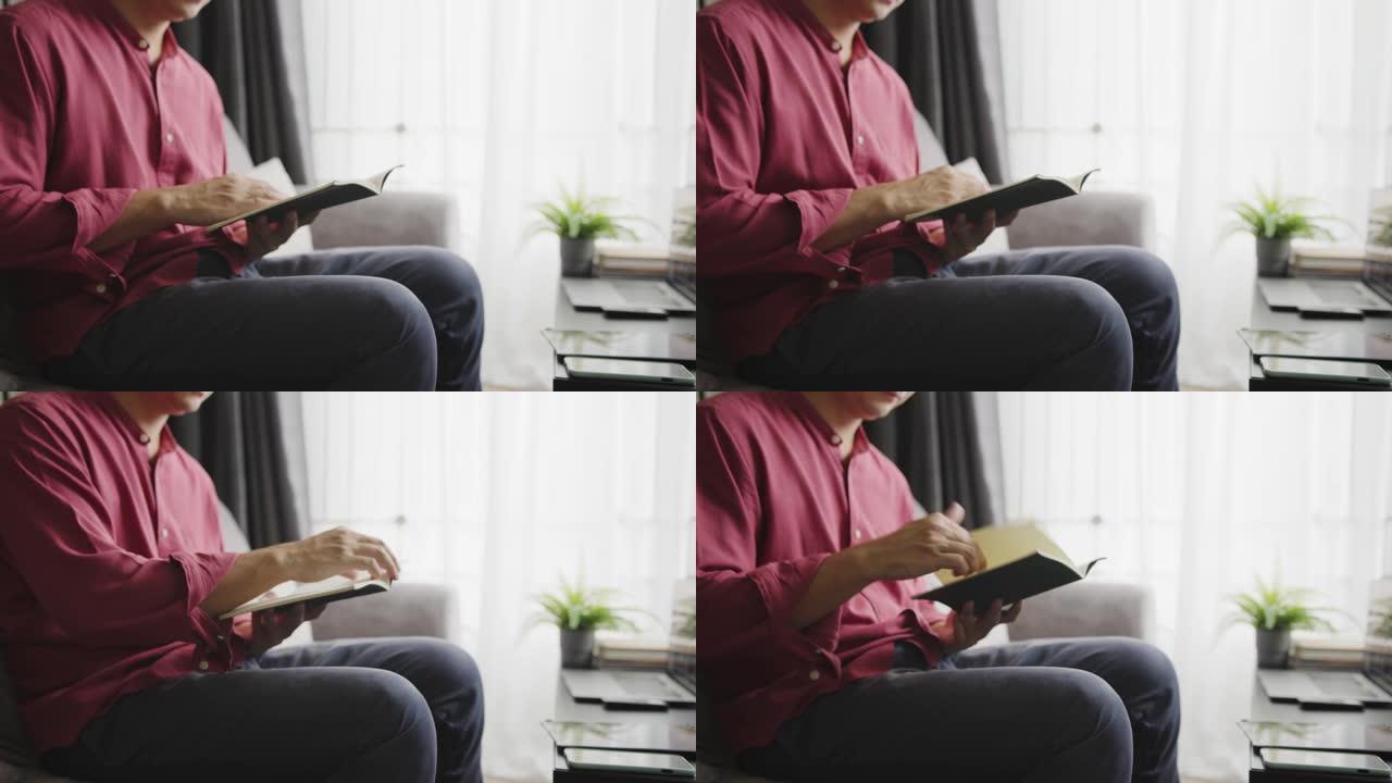 特写镜头亚洲男子双手在客厅看书。成年男性坐在沙发上在模拟书上学习历史。学习，知识，教育，在日常生活活
