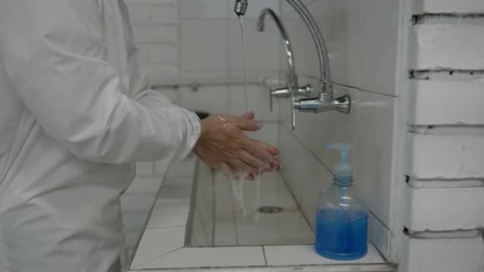 穿着生物安全服的面目全非的男子按照新型冠状病毒肺炎准则用水和肥皂洗手